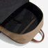 Open tan waxed canvas backpack showing a black fabric interior with a zippered pocket and a brown leather top handle.
