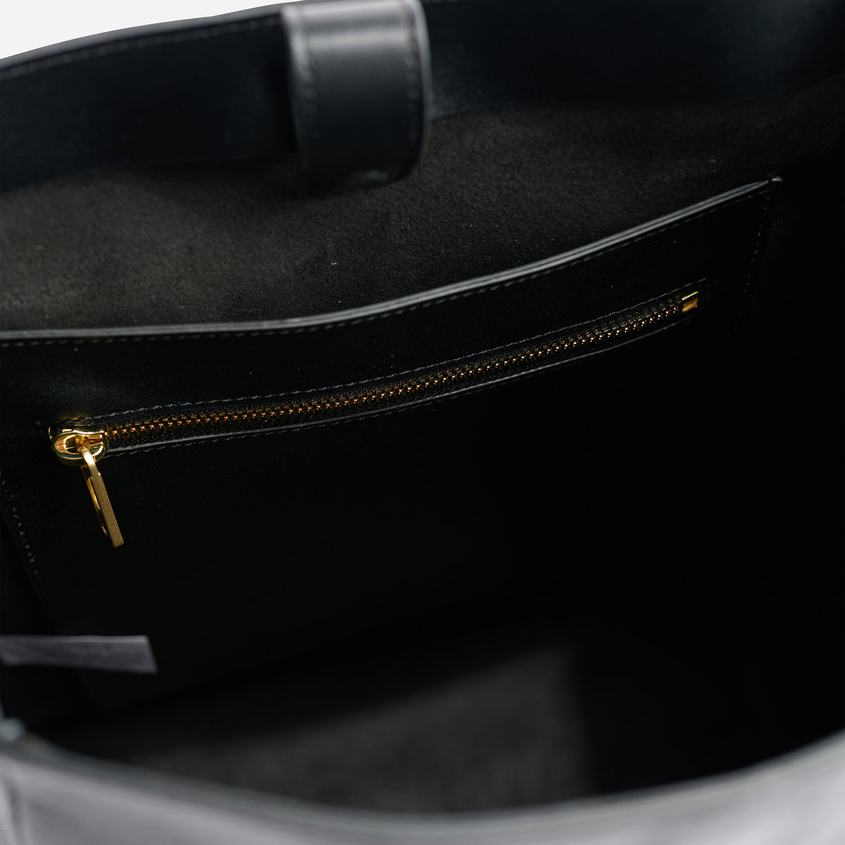 Interior view of a black leather bag featuring a zippered pocket with a gold-tone metal pull and a magnetic strap closure.