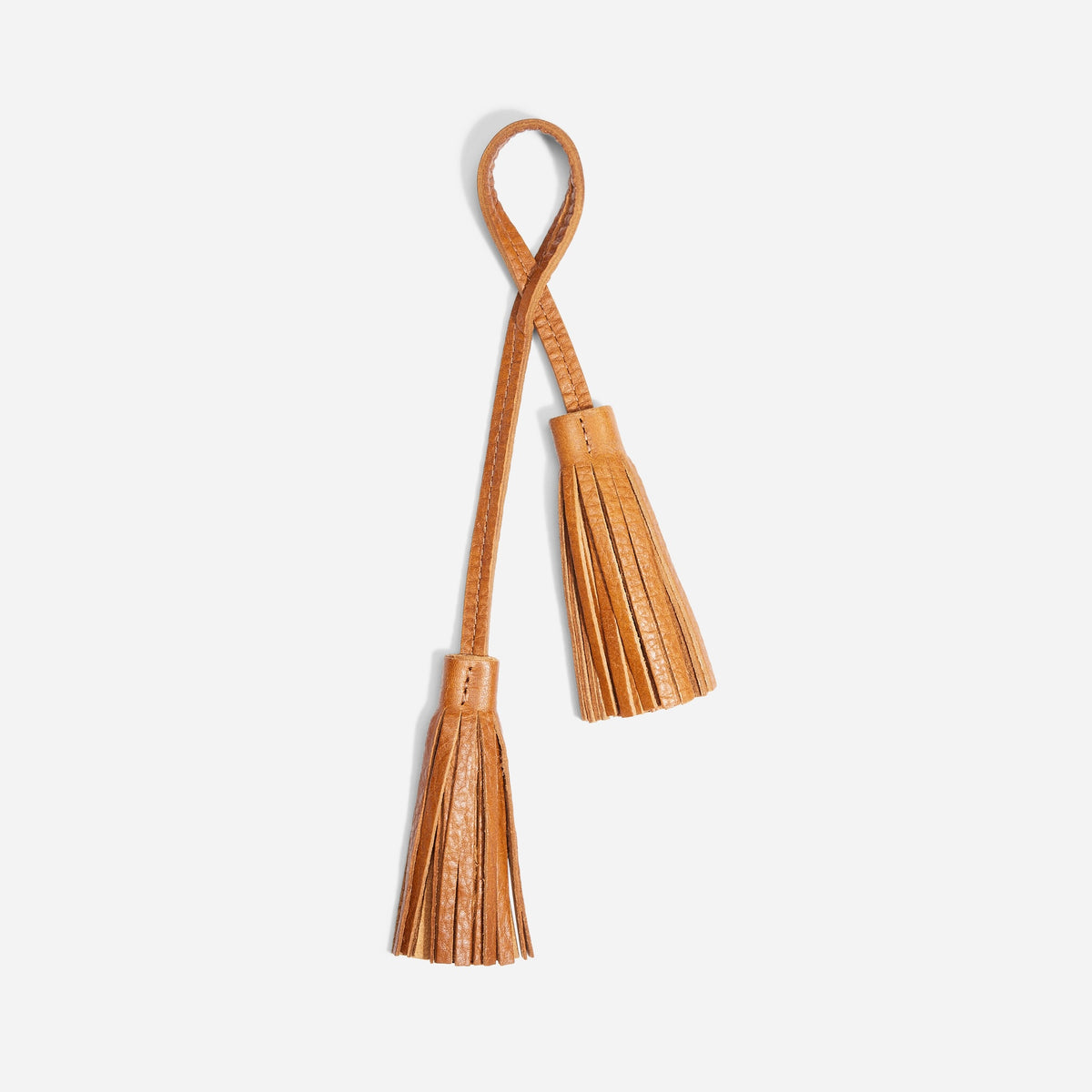 Tan leather double tassel bag charm with a looped strap and two fringed tassels on a white background.