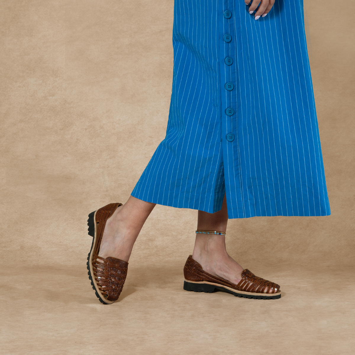 Brown woven leather huarache sandals with black lug soles worn with a blue pinstripe skirt.