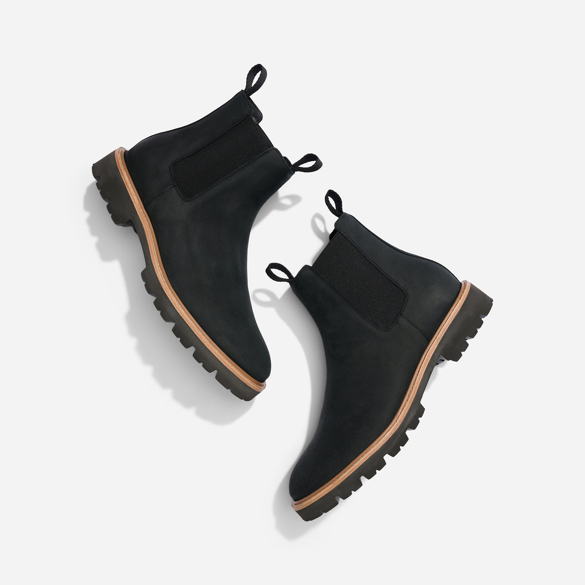 Pair of black leather Chelsea boots with lug soles and elastic side panels, shown from a top-down angle on a white backgro...