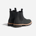 Pair of black leather Chelsea boots with tan midsoles, lugged outsoles, and fabric pull tabs on a white background.