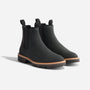 Pair of black matte Chelsea boots with elastic side panels, pull tabs, and tan welt stitching on lugged rubber soles.