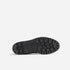Bottom view of a black lugged rubber boot sole featuring a textured tread pattern and an oval logo in the center.