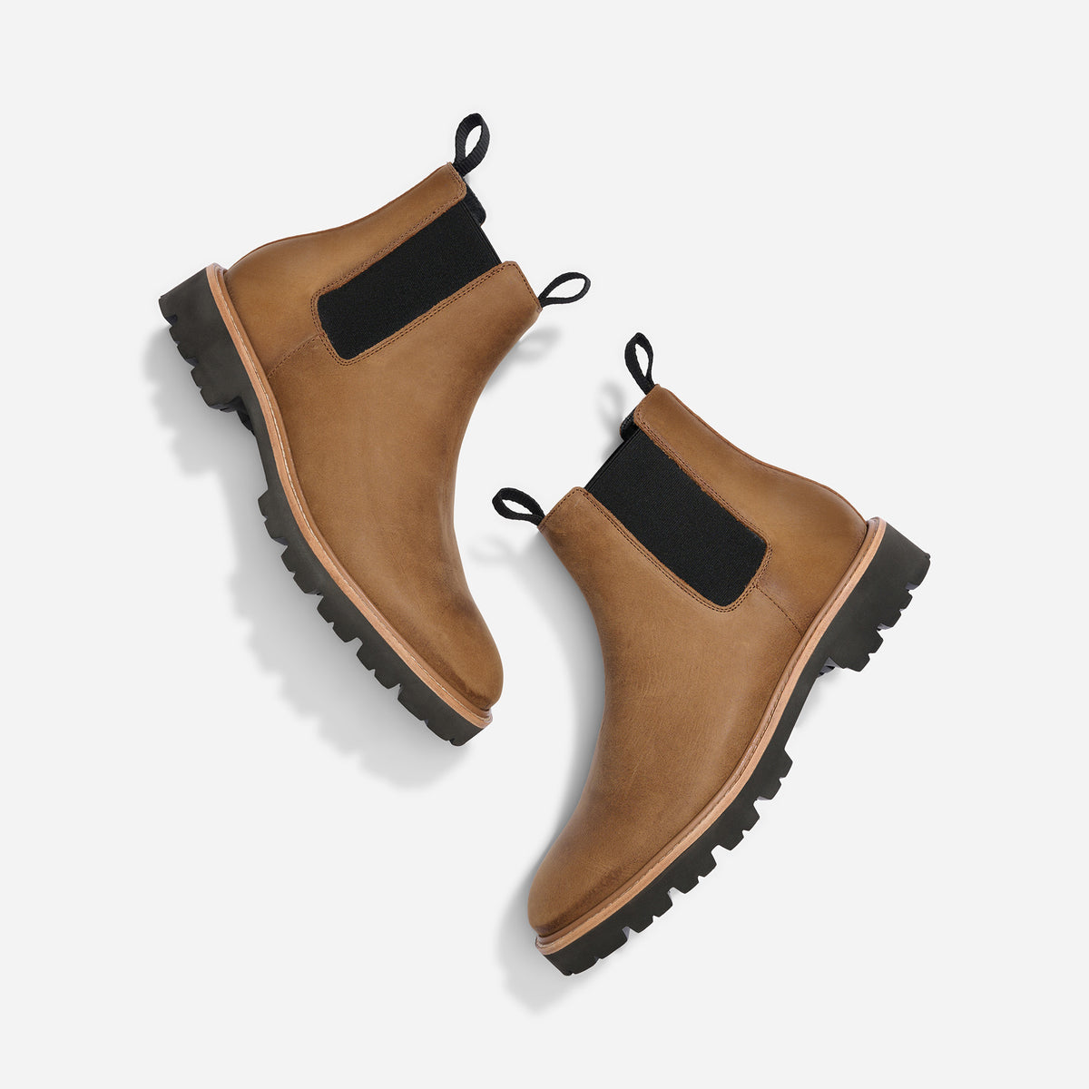 Pair of tobacco brown leather Chelsea boots with black elastic side panels and lugged soles on a white background.