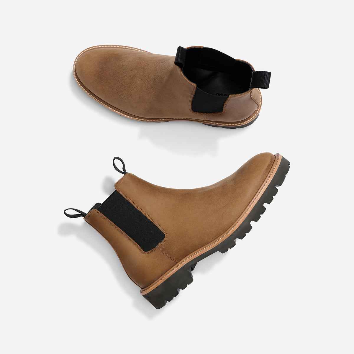 Pair of tobacco brown leather Chelsea boots with black elastic side panels and lugged soles on a white background.