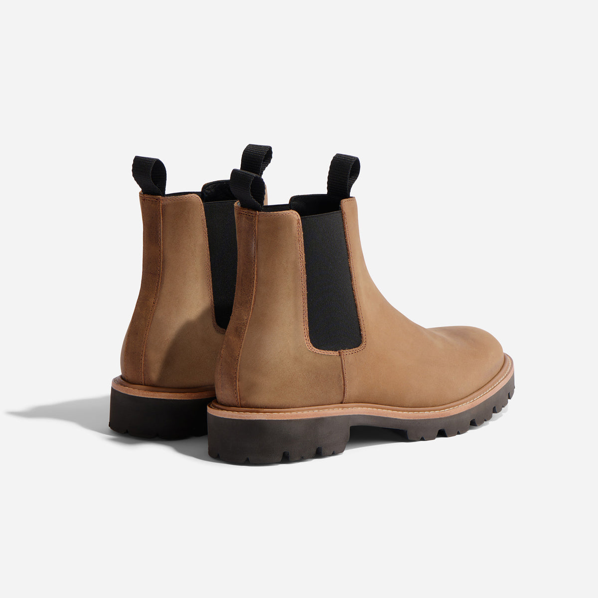 Pair of tobacco brown leather Chelsea boots with black elastic side panels and lugged soles on a white background.