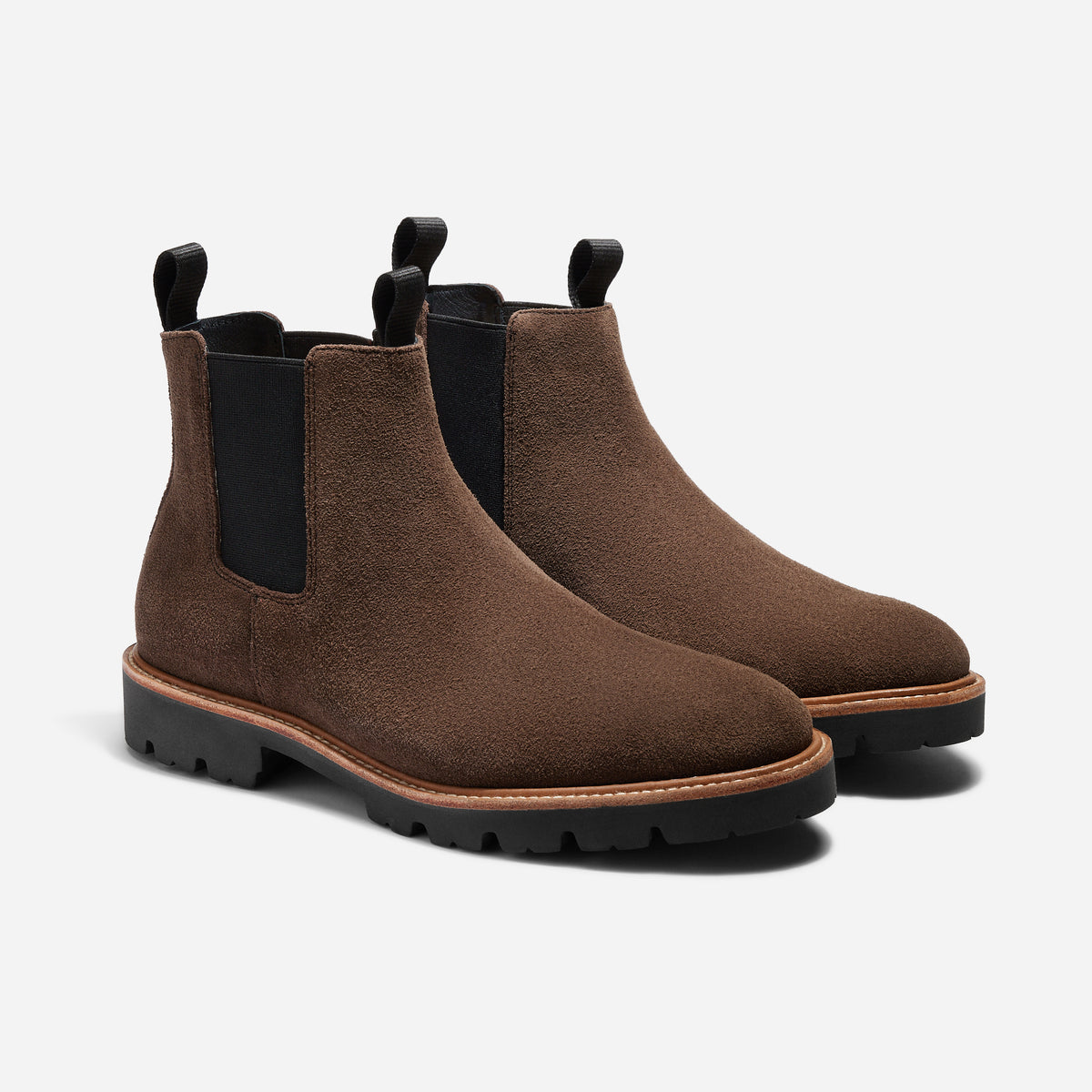 Pair of umber brown suede Chelsea boots with black elastic side panels and lugged rubber soles on a white background.