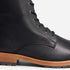 Close-up of a black leather boot with metal eyelets, black laces, and a light brown lug sole.