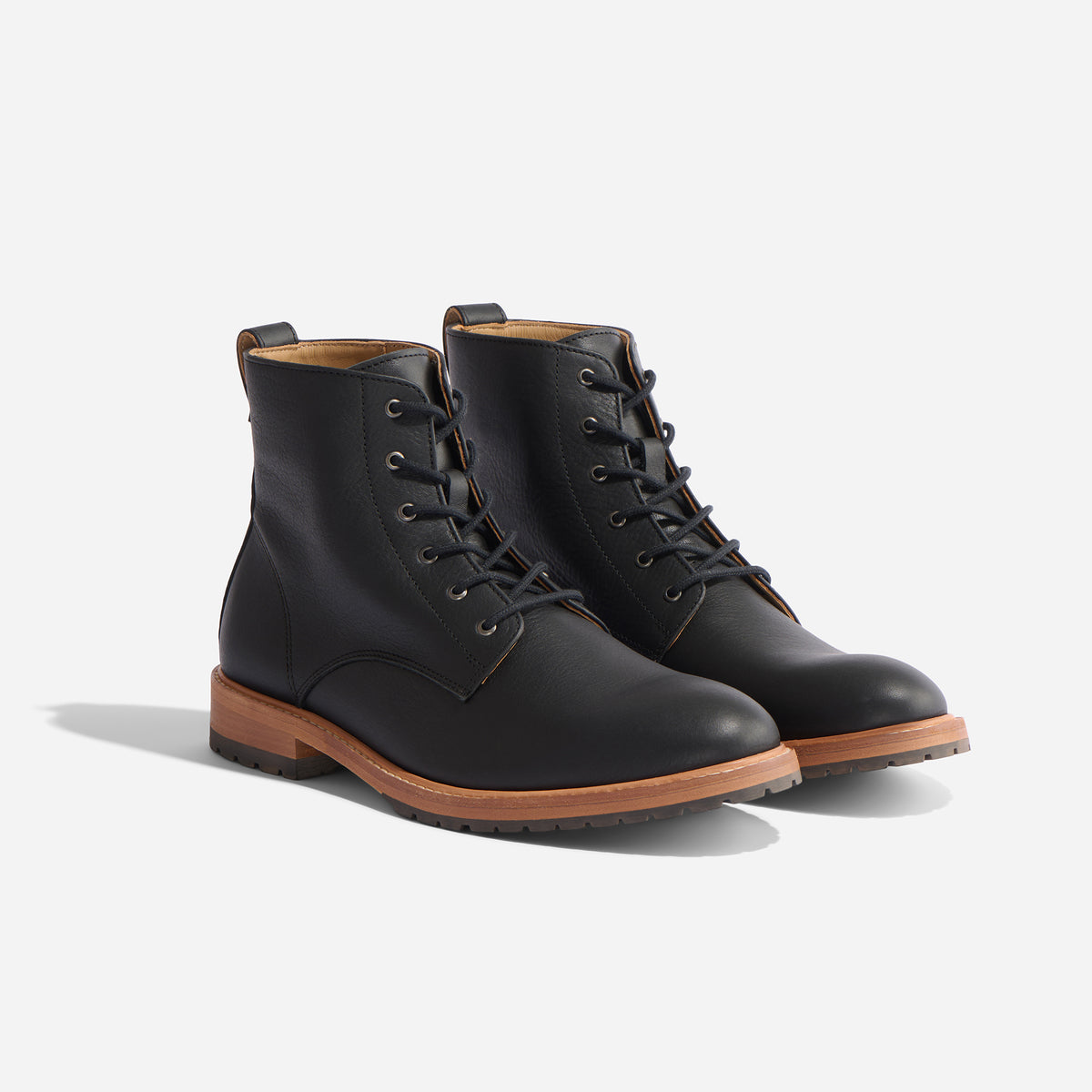 Pair of black leather lace-up boots with tan midsoles and black lug outsoles, shown from a side angle on a white background.
