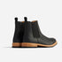 Pair of black leather Chelsea boots with tan midsoles and black lug outsoles, shown from a rear three-quarter angle.