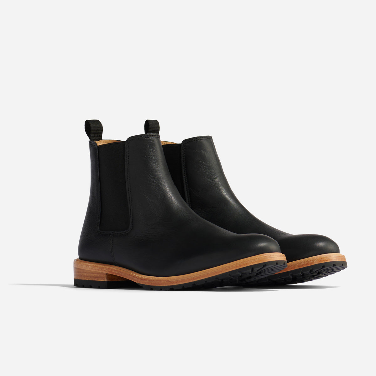 Pair of black leather Chelsea boots with tan wood-look midsoles and black lug soles on a white background.
