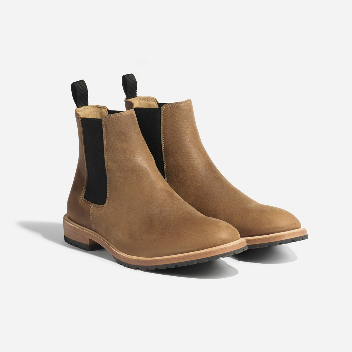 Pair of tobacco brown leather Chelsea boots with black elastic side panels and pull tabs on a white background.