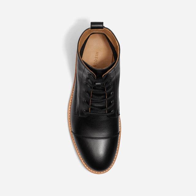 Top-down view of a single black leather cap toe boot with black laces and a tan NISOLO label on the inner heel.
