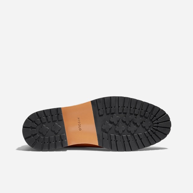 Bottom view of a shoe featuring a black lugged rubber sole and a brown center section with the NISOLO brand name.
