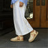 Pair of bone-colored leather huarache T-strap espadrille sandals with woven toes and jute soles worn with white pants.