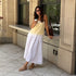 Woman wearing almond Huarache T-Strap Espadrille Sandals, a white skirt, and yellow top while leaning against a stone wall.