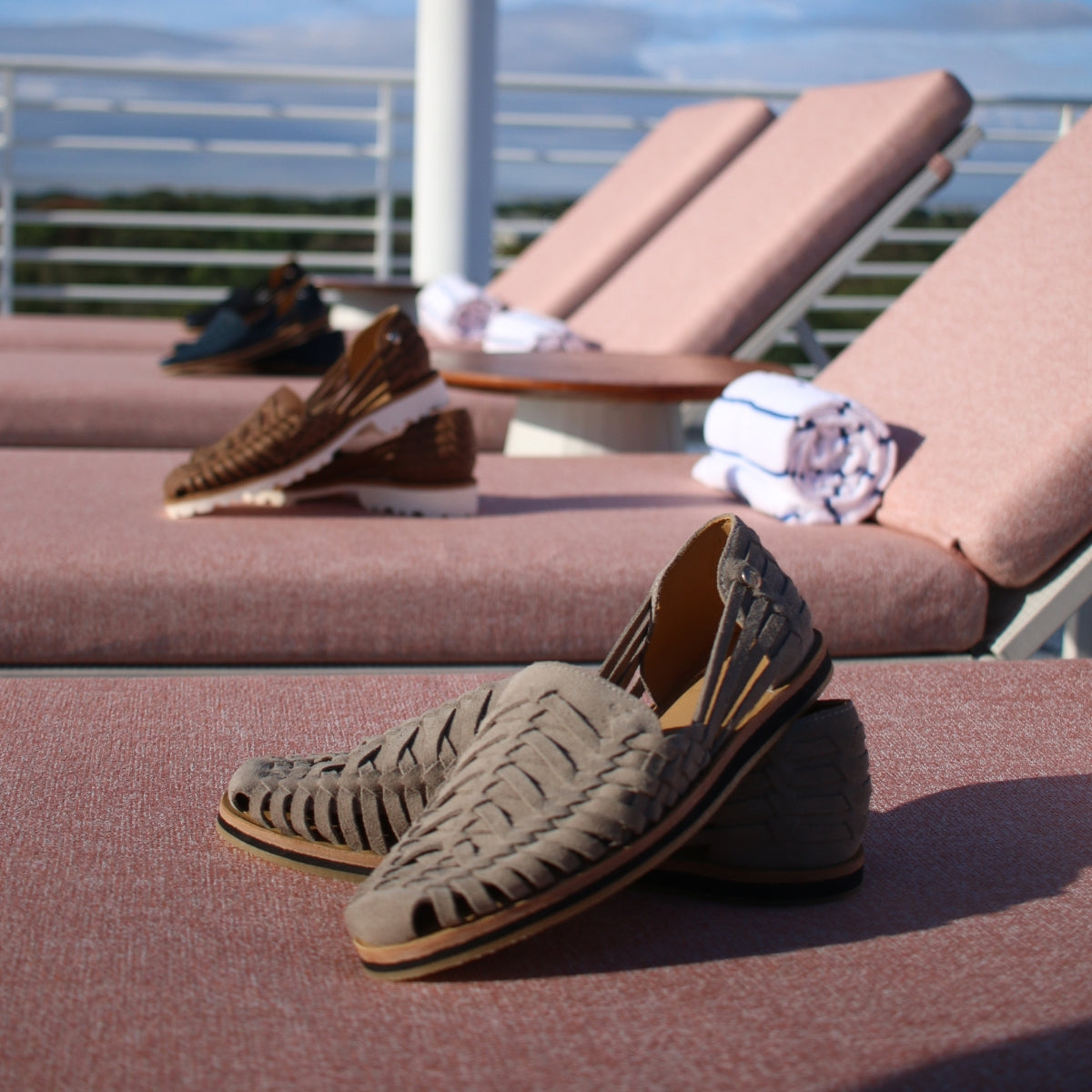 Pair of greige woven leather Huarache sandals resting on a pink lounge chair outdoors.