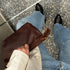 Rectangular dark red textured pouch with a tassel zipper pull held over blue denim jeans and black shoes.