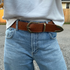 Brown textured leather belt with a gold-tone horseshoe buckle and metal tip worn on blue denim jeans.