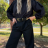 Black leather Bonnie Belt with a gold-tone buckle and metal accents worn on black trousers.