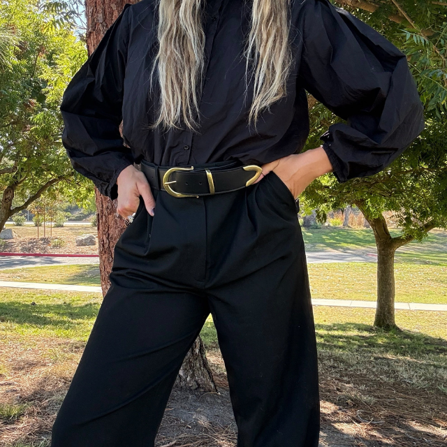 Black leather Bonnie Belt with a gold-tone buckle and metal accents worn on black trousers.