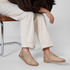 Pair of almond tan woven leather huarache booties with laces worn with white pants.