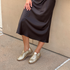 Pair of gold woven leather huarache booties with laces worn with a black skirt.