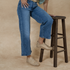 Pair of tan woven leather huarache booties worn with blue jeans, with one foot resting on a dark wood stool.