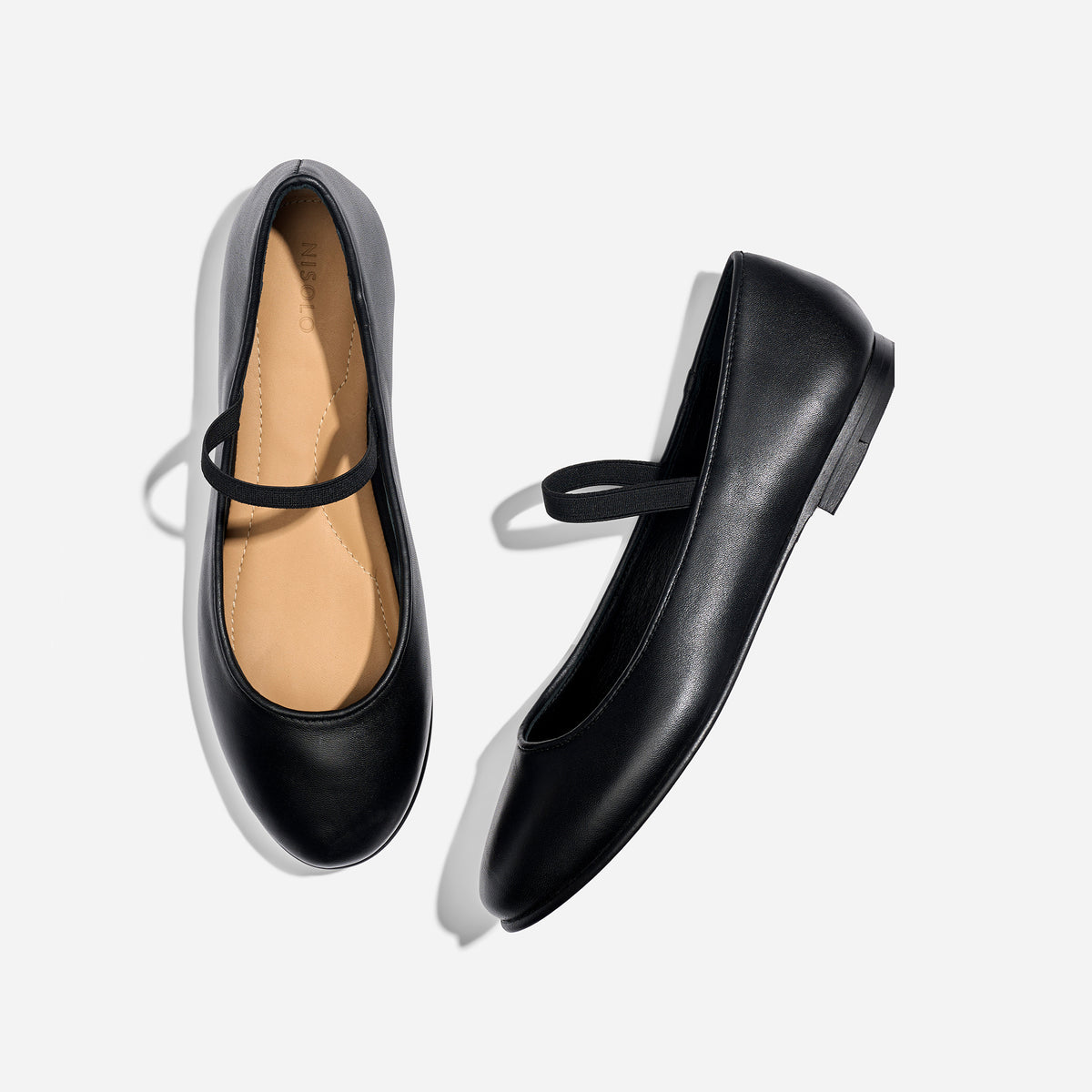 Pair of black leather Mary Jane flats with elastic straps and NISOLO printed on the tan insoles.