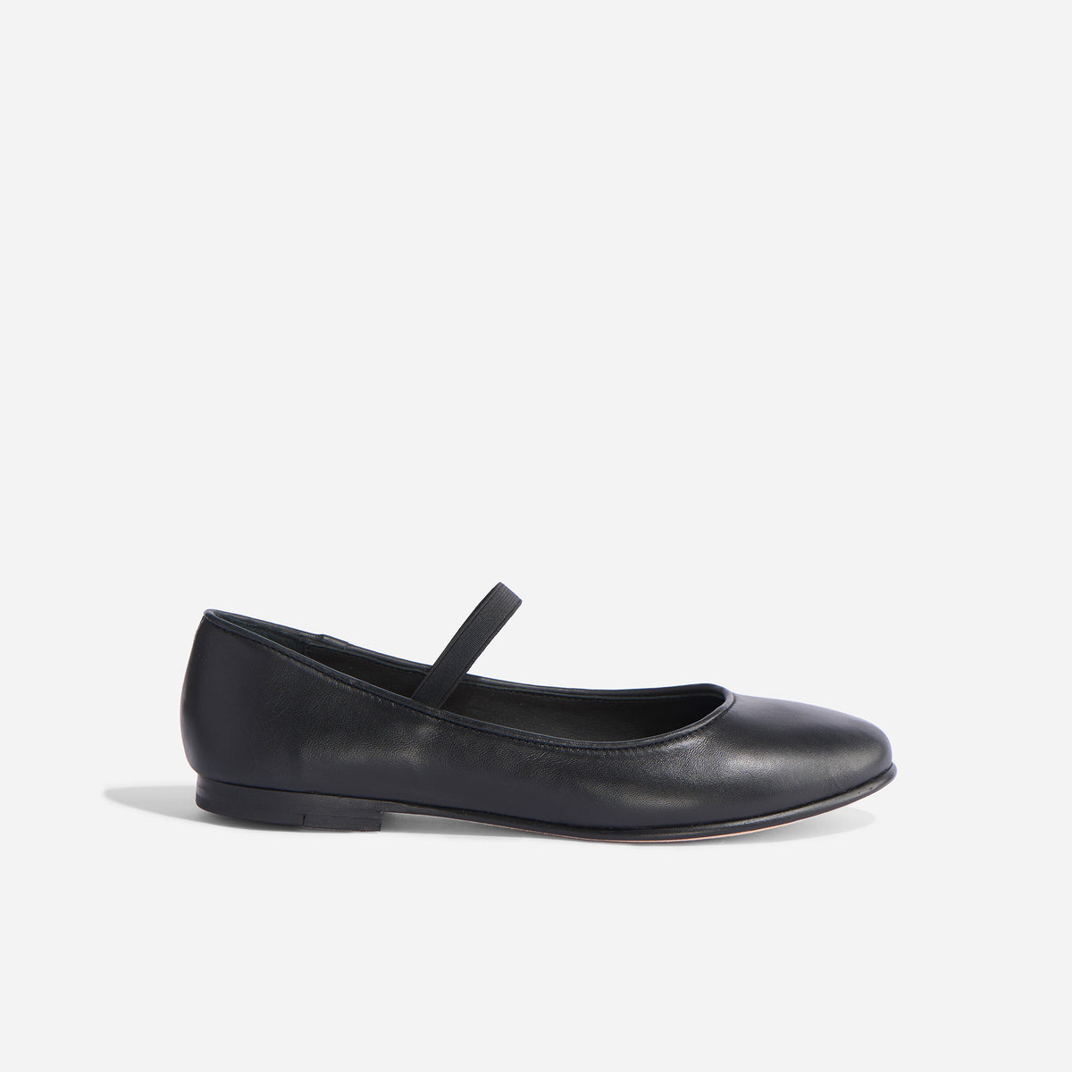 Single black leather Mary Jane flat with a round toe and thin elastic bridge strap shown in profile.
