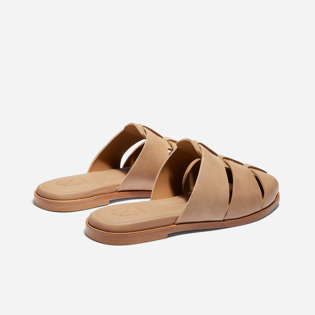 Pair of tan leather fisherman mules with woven straps and flat soles, featuring the NISOLO logo on the footbed.