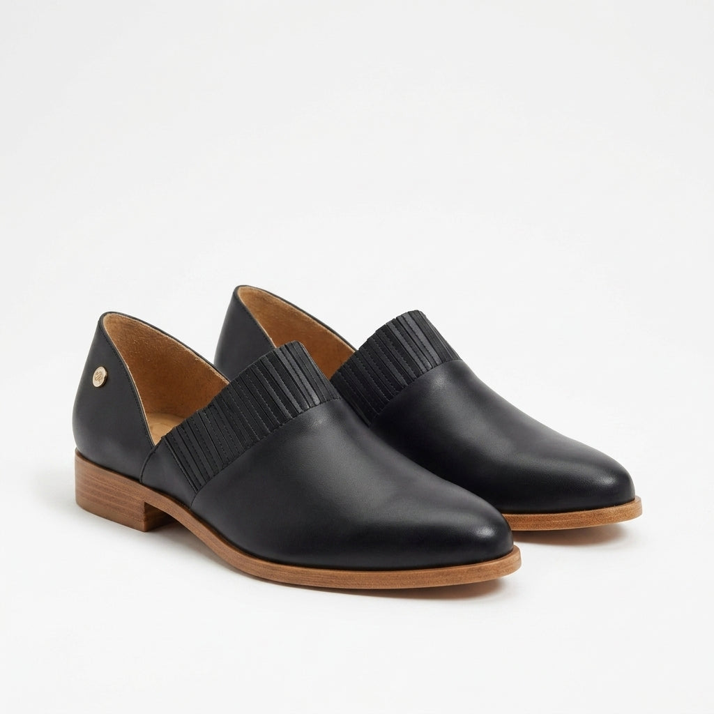 Pair of black leather slip-on oxford shoes with pleated fabric details and tan wood-tone soles on a white background.