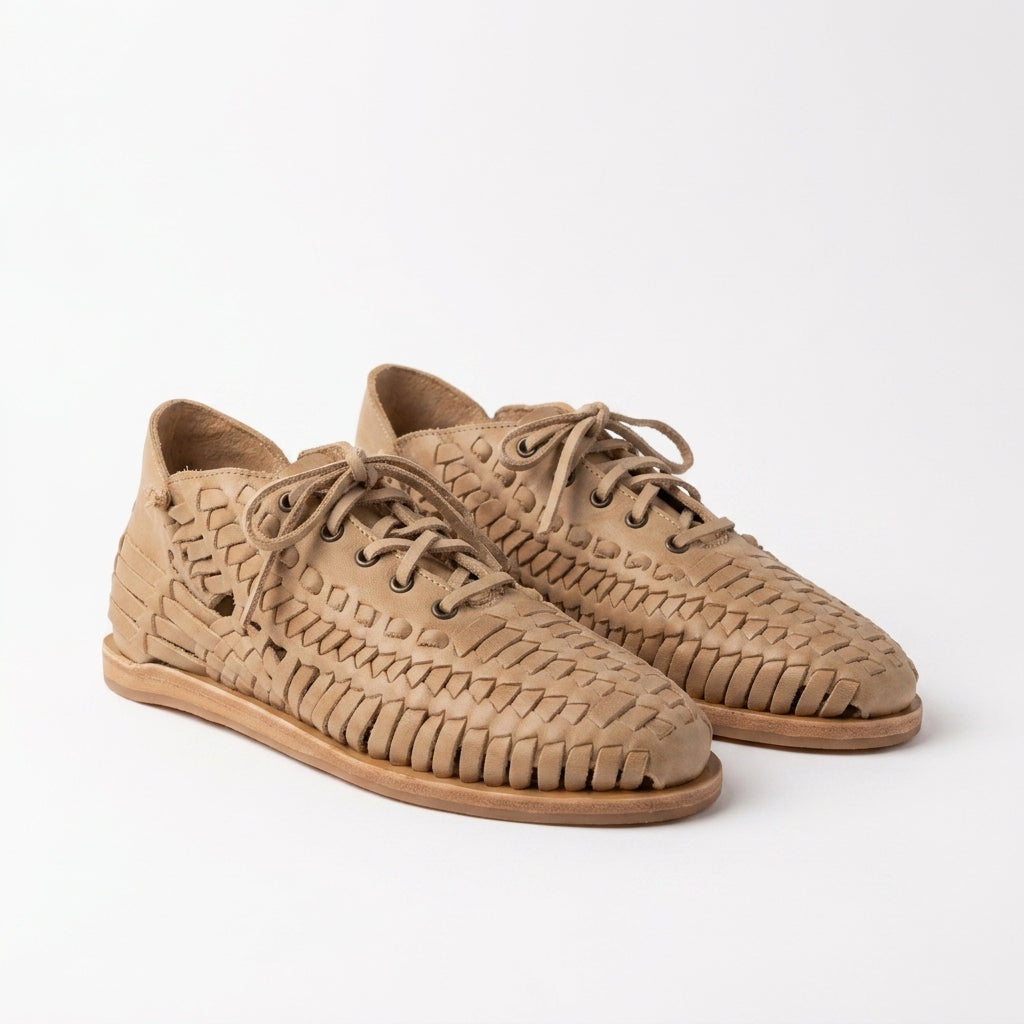 Pair of almond tan woven leather huarache booties with laces on a white background.