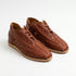 Pair of brandy brown woven leather Huarache booties with laces and tan soles on a white background.