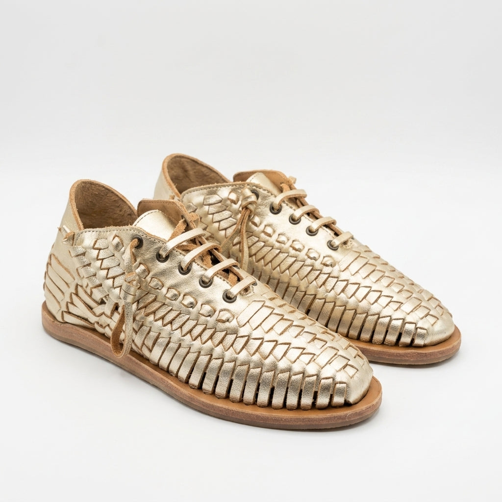Pair of gold woven leather huarache booties with tan laces and flat brown soles on a white background.