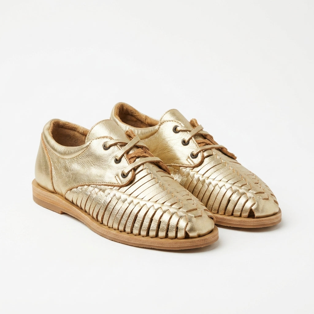 Pair of gold metallic leather huarache oxfords with woven straps and tan laces on a white background.