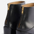 Rear view of two black leather Dari Boot 2.0 shoes featuring gold-tone metal zippers with leather pull tabs.