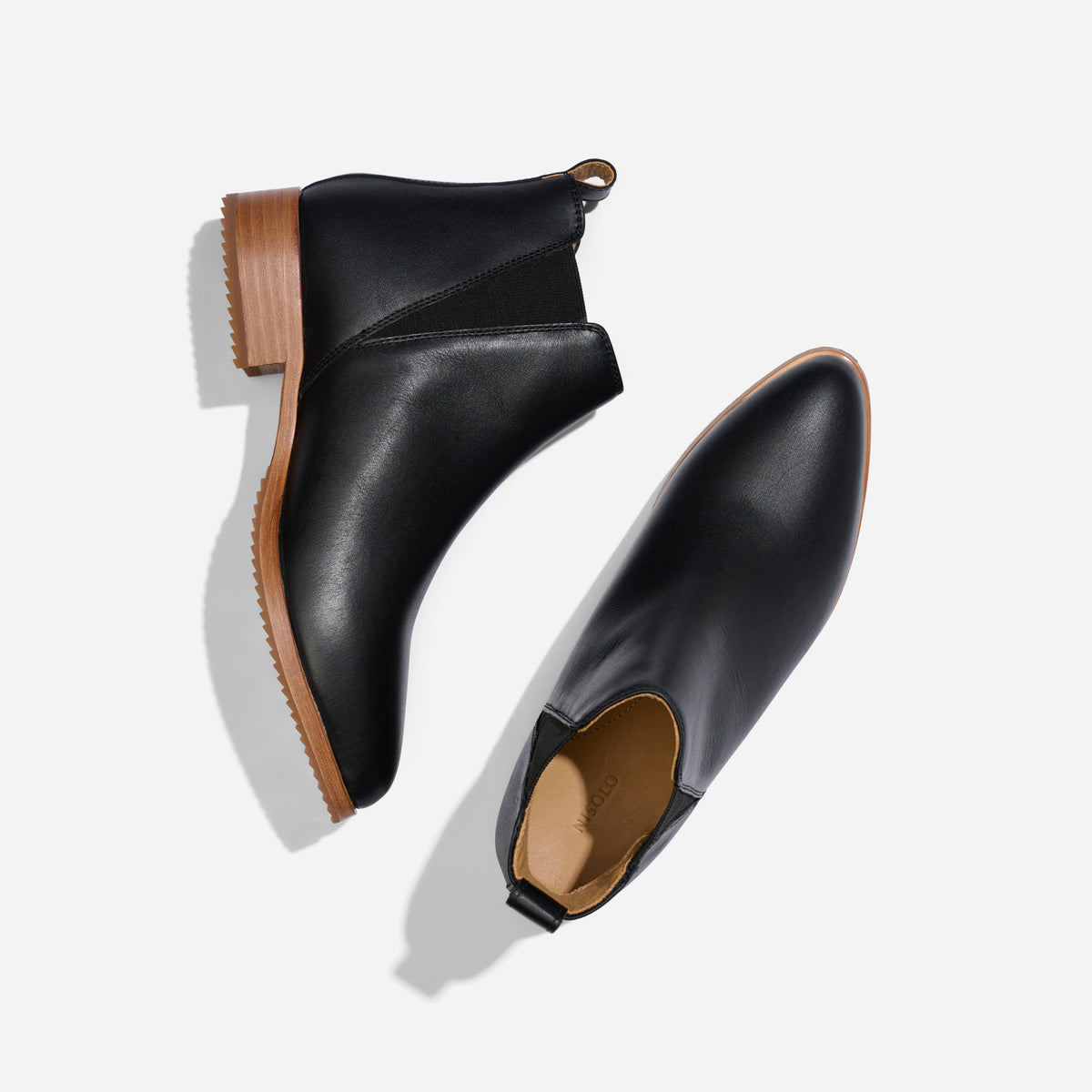 Pair of black leather Eva Everyday Chelsea Boots with brown soles and NISOLO printed on the tan interior.