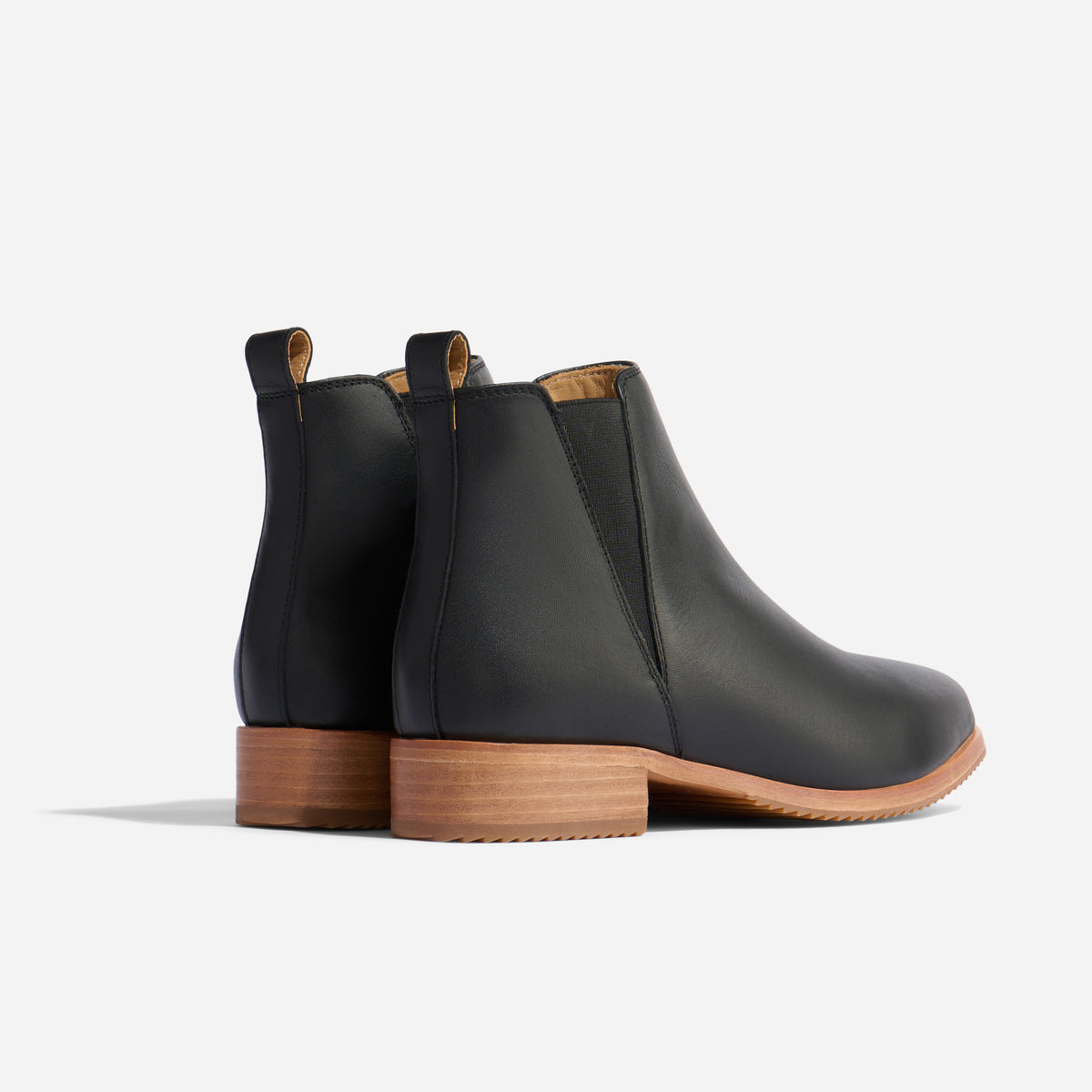 Pair of black leather Eva Everyday Chelsea boots with tan soles and elastic side panels on a white background.