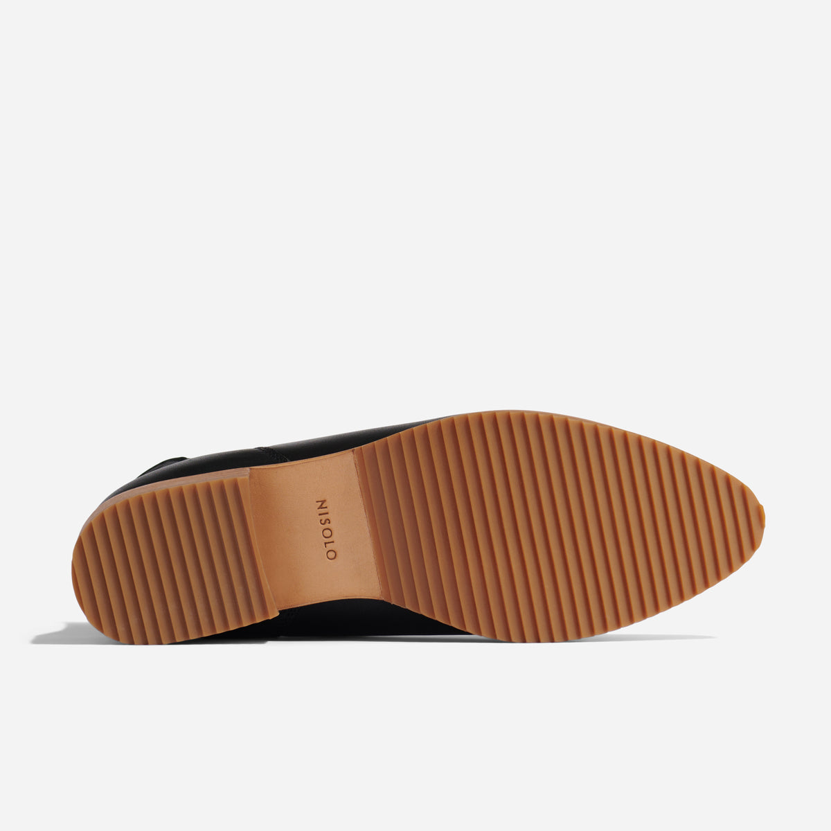 Bottom view of a black leather boot showing a tan ridged rubber sole with the NISOLO brand name printed in the center.
