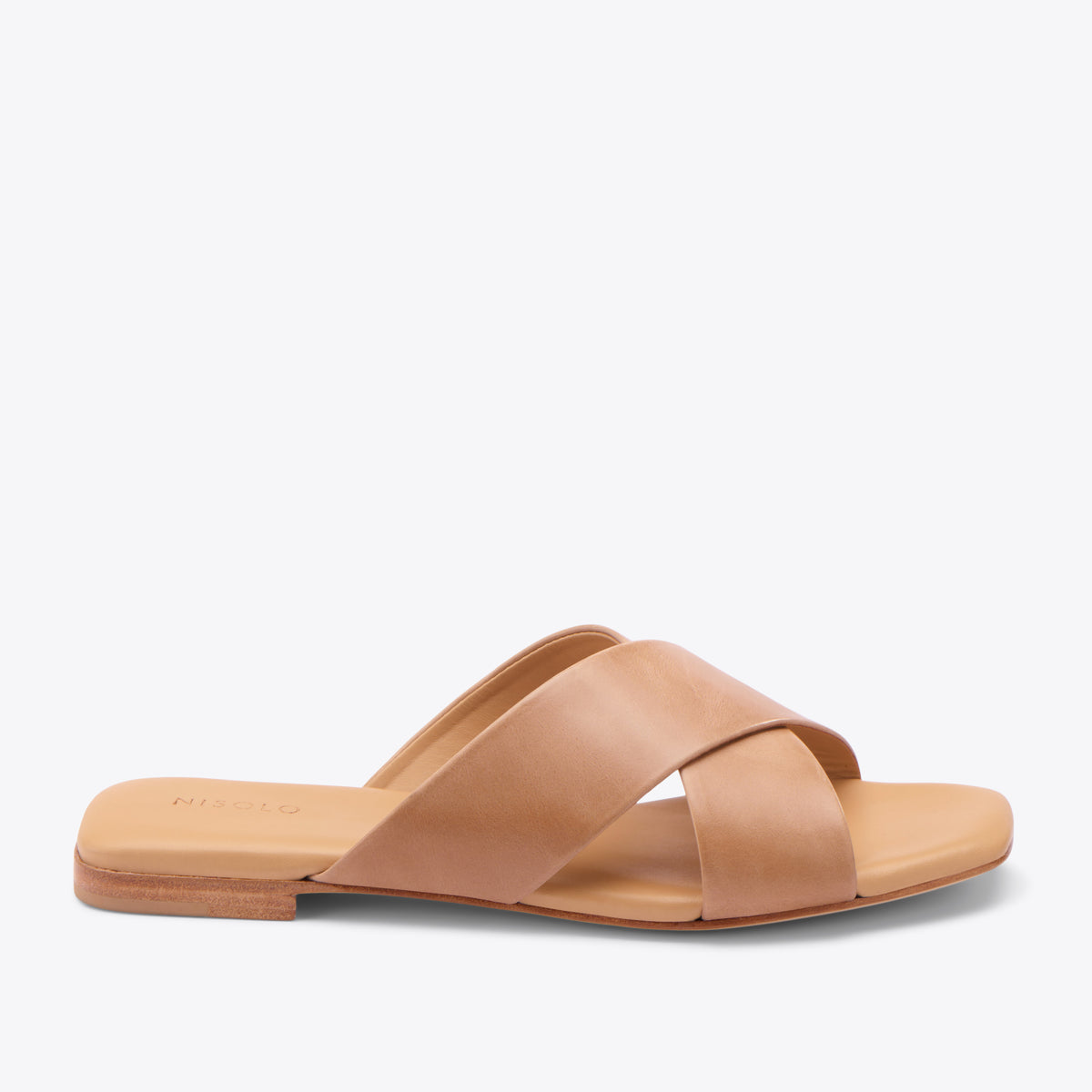 Single almond leather slide sandal with two wide crisscross straps and NISOLO printed on the footbed.