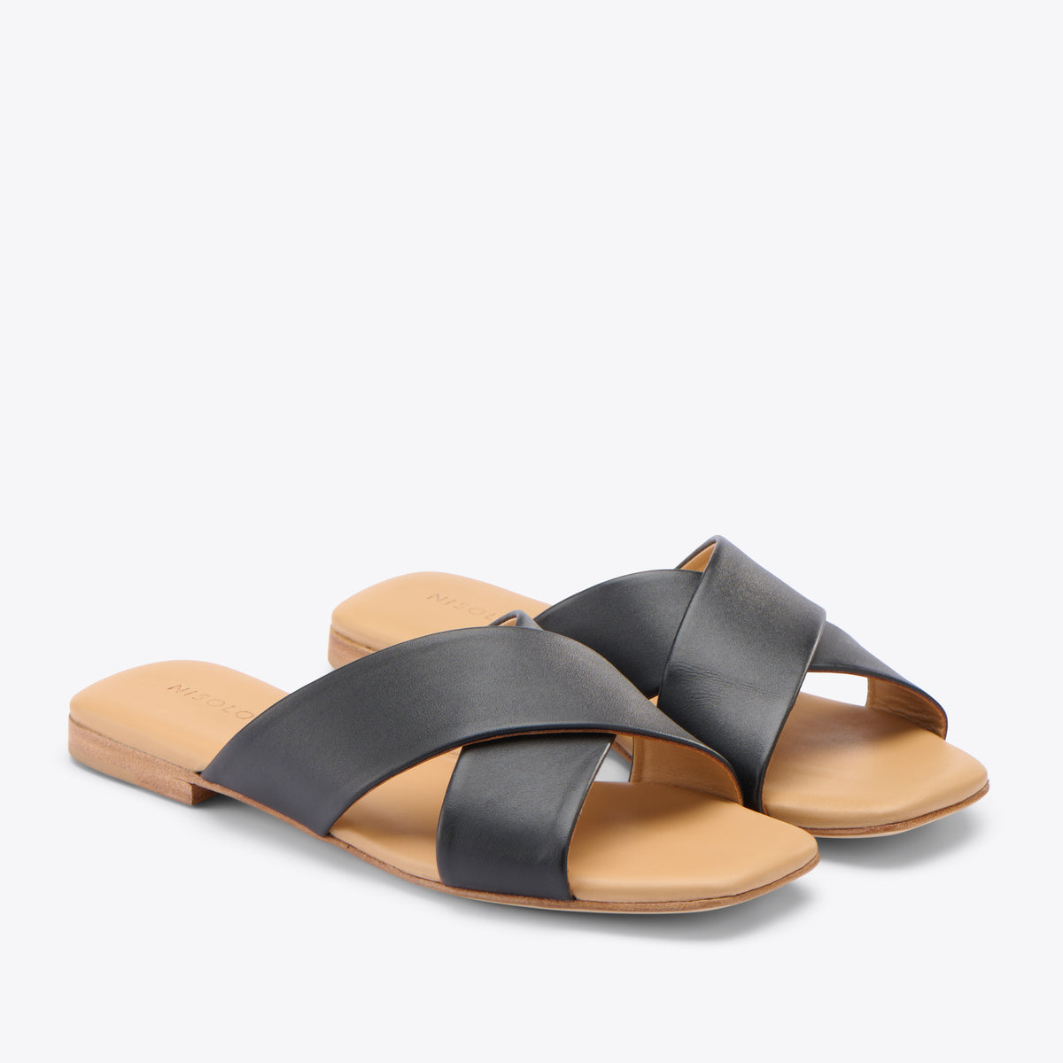 Pair of black leather slide sandals with crisscross straps and tan soles featuring the NISOLO logo.