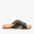 Single black leather slide sandal with crisscross straps and a tan footbed featuring the Nisolo logo.