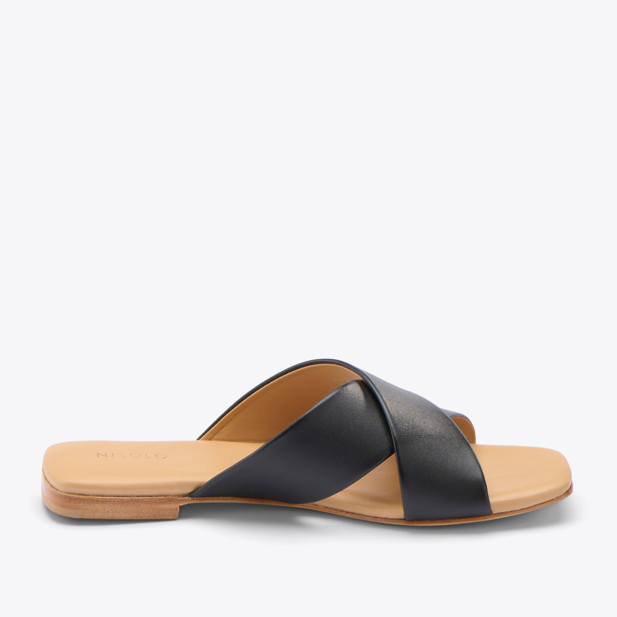 Single black leather slide sandal with crisscross straps and a tan footbed featuring the Nisolo logo.