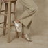 Pair of gold woven leather Huarache Oxford shoes worn with tan trousers next to a wooden stool.