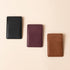 Three rectangular leather card cases in black, burgundy, and brown arranged diagonally with the NISOLO logo.