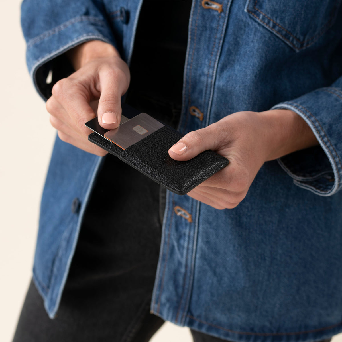 A person holds a black pebbled leather Nico Card Case while sliding out a silver credit card.