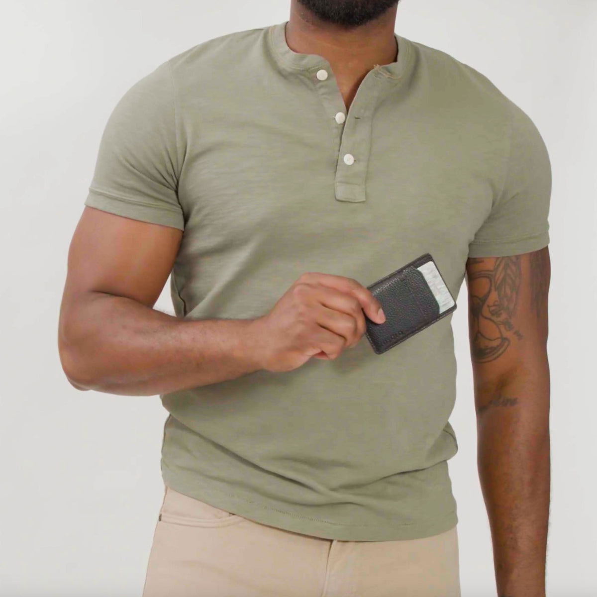 A person holds a black pebbled leather Nico card case wallet containing two white cards against a green henley shirt.