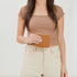 A woman holds a square caramel leather Remi Zip Wallet with a gold zipper against a white background.